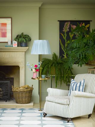 green living room with painted ceiling, blue rug, blue striped armchair, plants, mantel, artwork, pale blue lampshade on floor lamp