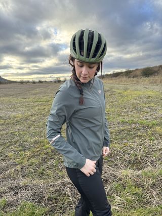 Side profile of woman in sage green jacket wearing green helmet. In a field.