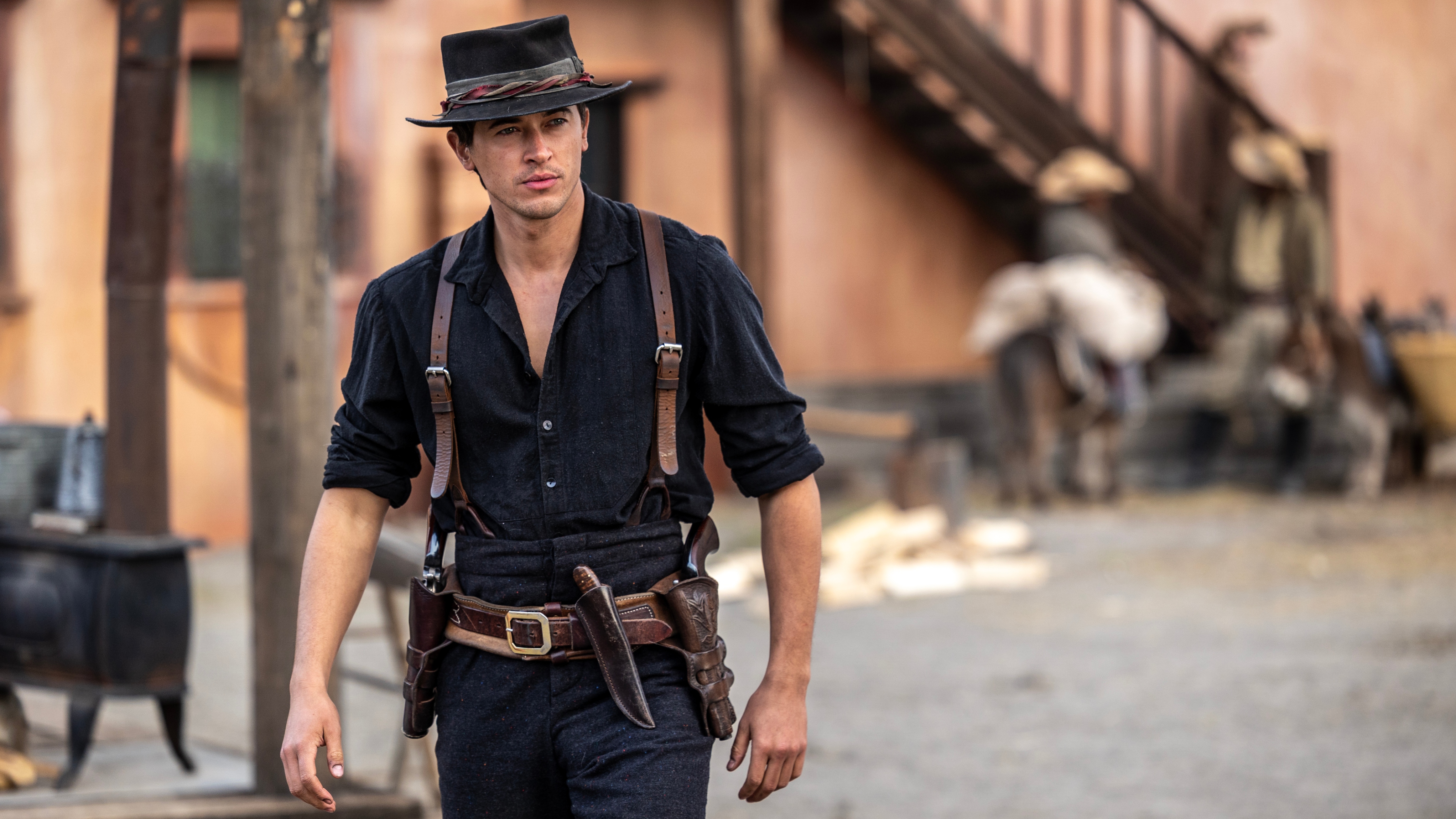 Tom Blyth as Billy the Kid walking through a Western town in Billy the Kid season 3.