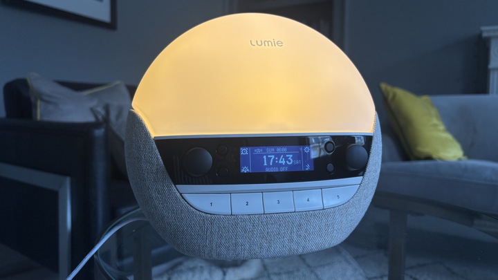 Lumie Bodyclock Luxe 700FM sunrise alarm clock lighting a dark room with its warm glow.