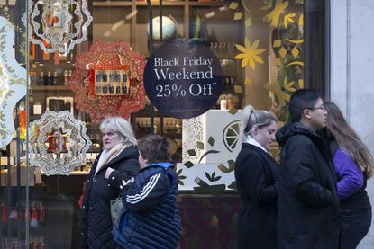Shoppers walk past a Black Friday deals sign on a storefront window.