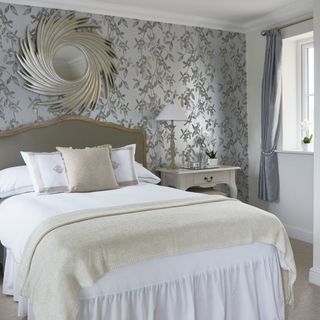 bedroom with leafy print wallpaper and sunburst mirror