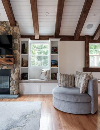 A living space with a stone fireplace, built-in window shelving, and a gray swivel accent chair