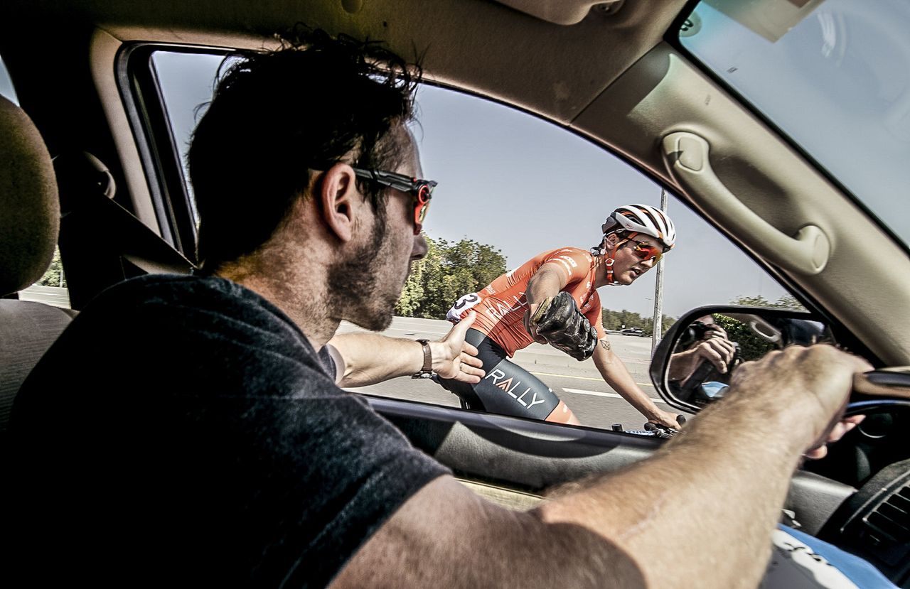 Adam de Vos hands Eric his shoe who in-turn passes it over to Tim the mechanic in the back who attempts to adjust the cleat.