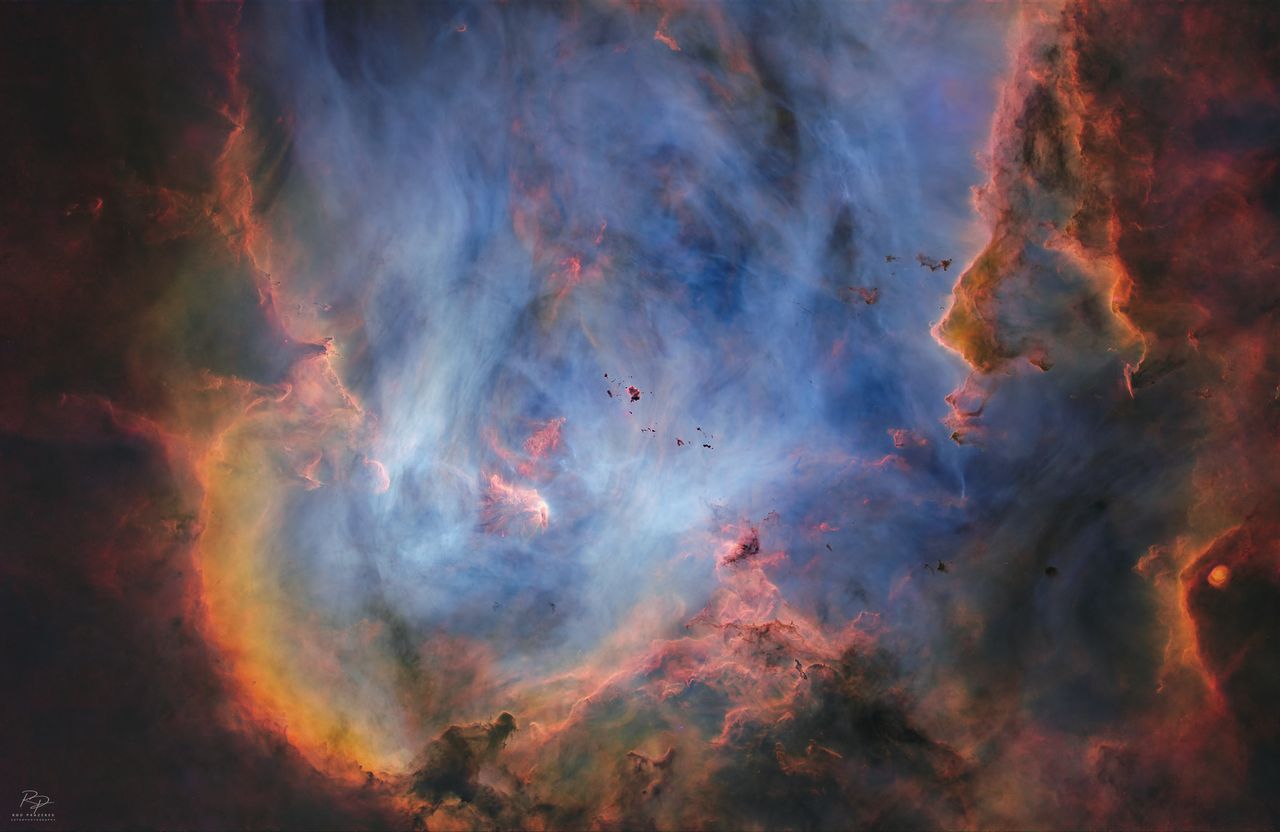 A deep space nebula scene is shown, featuring swirling masses of colorful interstellar gas and dense, dark dust filaments.