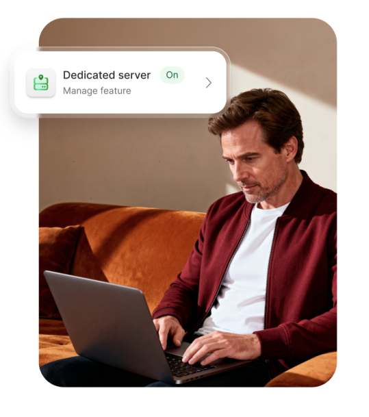 Man sat on a sofa using laptop, NordVPN's dedcated server feature enabled on upper left corner