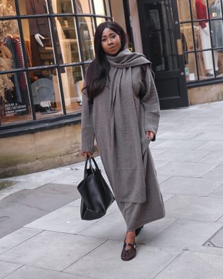 Influencer wears an outfit in a warm grey colour whilst walking on the street