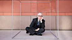 An unhappy businessman wearing a suit sits cross-legged inside a box.