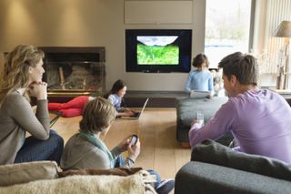 A family watches content on multiple screens in their living room.