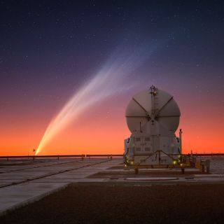 Comet G3 (ATLAS) approaches the horizon line of a fiery sky with its long, streaky tail in full display. In the foreground is part of the Paranal Observatory, Chile.