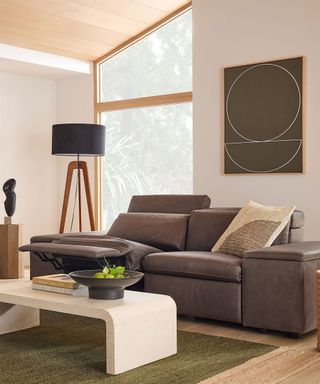 Reclining leather sofa in modern, bright living room, large floor lamp, artwork on wall, marble coffee table