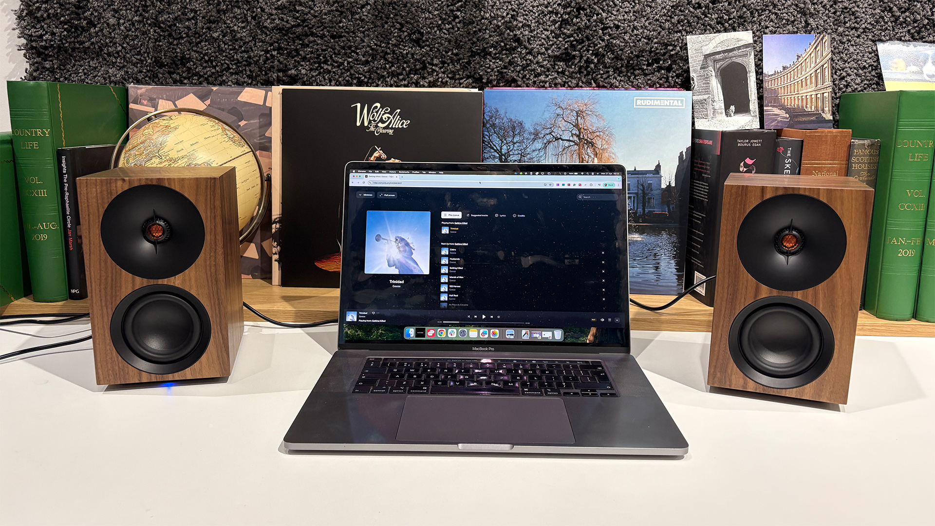 Cambridge Audio L/R S desktop speakers on white surface in front of busy bookcase flanking laptop