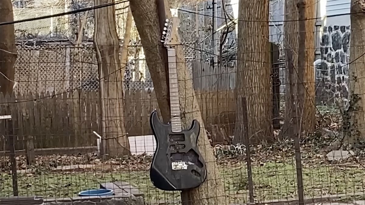 A battered Squier Strat zip tied to a garden fence