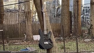 A battered Squier Strat zip tied to a garden fence