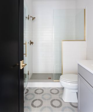 Small white bathroom with brass fixtures, circular geometric floor tiles