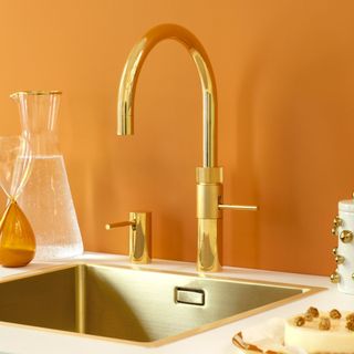 Gold boiling water tap on white countertop in orange kitchen