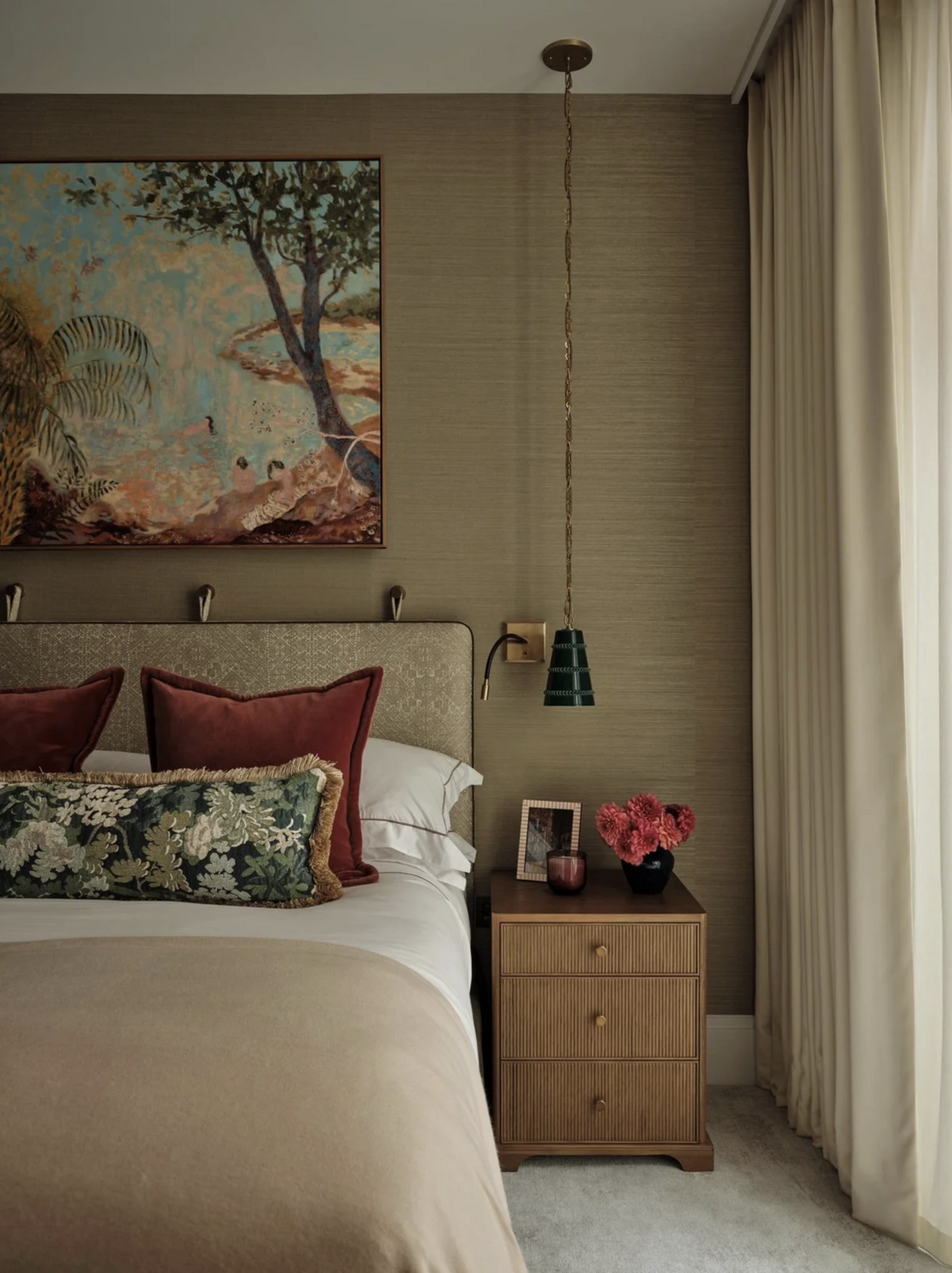 grasscloth wallpaper, upholstered bedframe with throw cushions, rattan bedside tables, pendant lights hanging from above, curtains, and large artwork