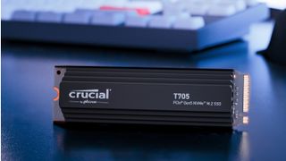 Photograph of Crucial T705 solid state drive with keyboard visible in background, on dark-coloured desk