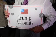 A man holds a Trump Accounts sign that has the American flag and quarters on it