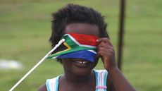 A child covers her face with a South African flag
