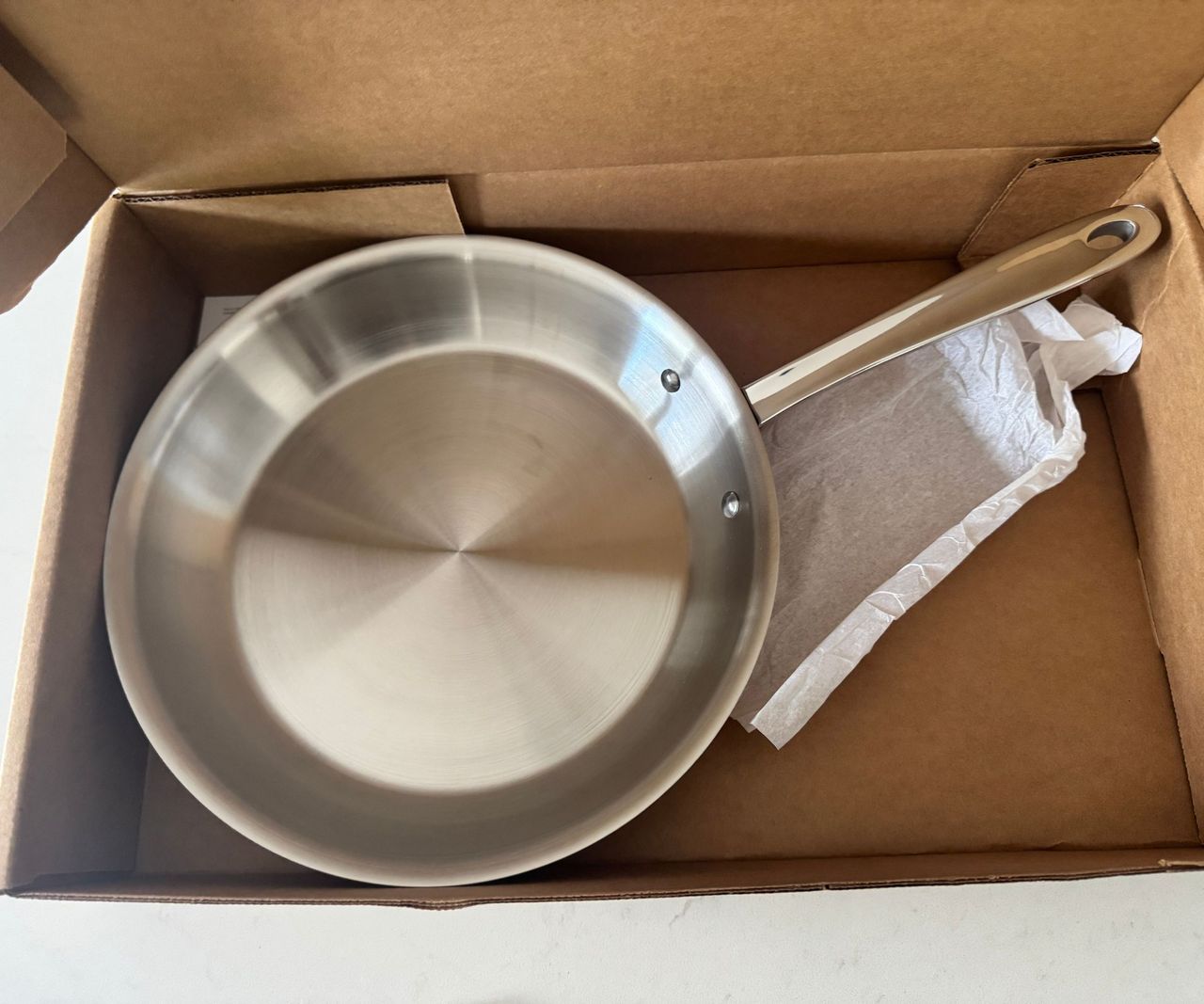 A stainless steel frying pan inside a cardboard box.