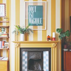 A living room with a wall painted in yellow and cream stripes with a yellow fireplace