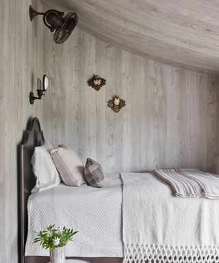 A guest bedroom with grey faux bois wallpaper on the walls and sloping eaves ceiling