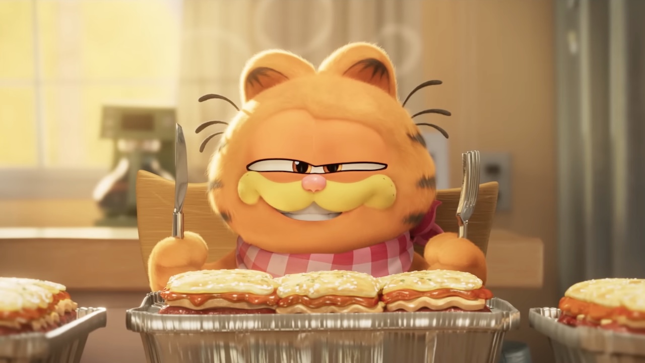 Garfield holding knife and fork and about to eat lasagna in the 2024 movie