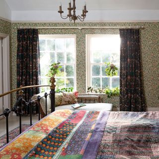 double wrought iron and brass bed with bright quilts and leafy patterned wallpaper and curtains