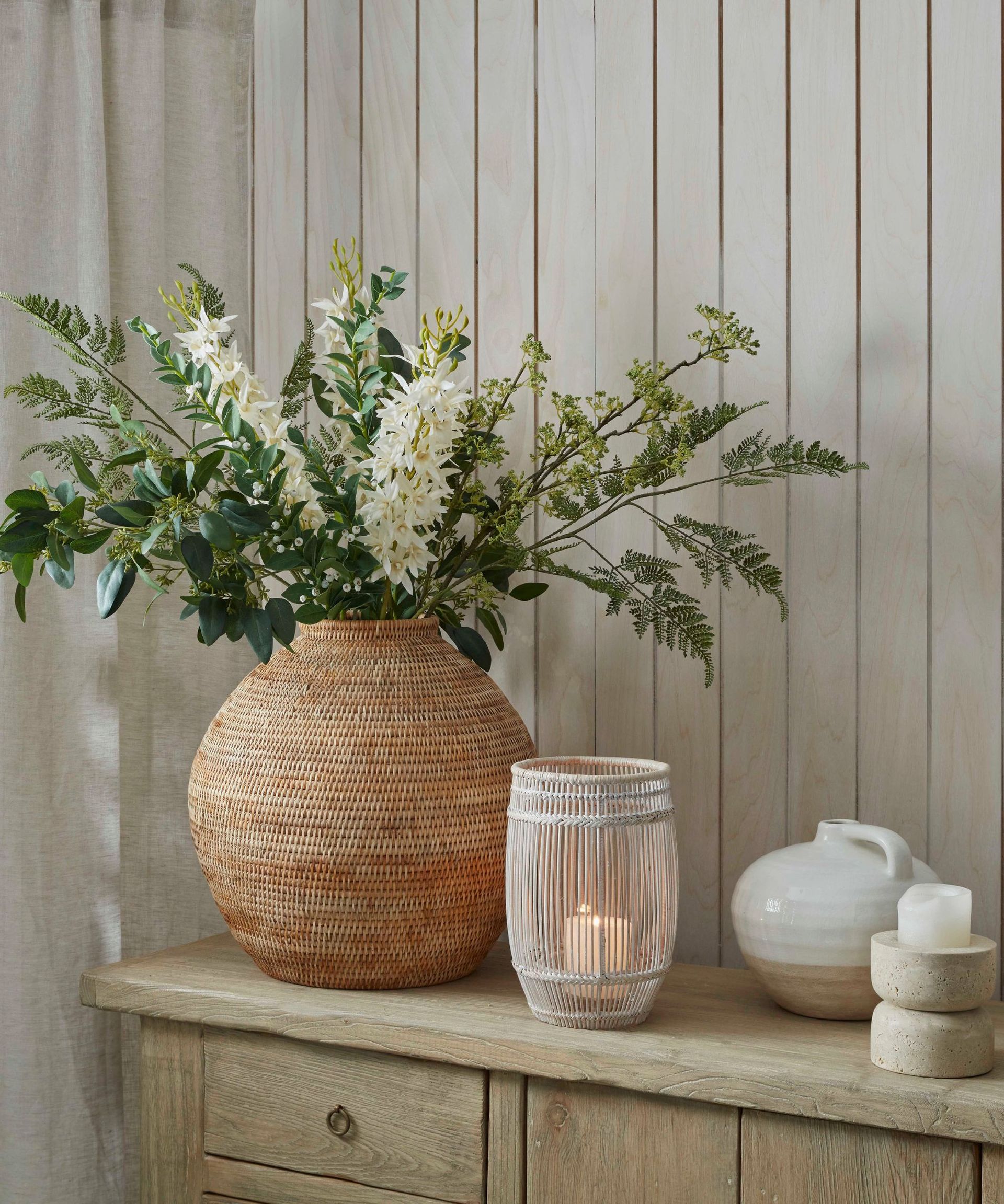A large vase of white spring flowers on a hallway side table beside a small wicker candle holder