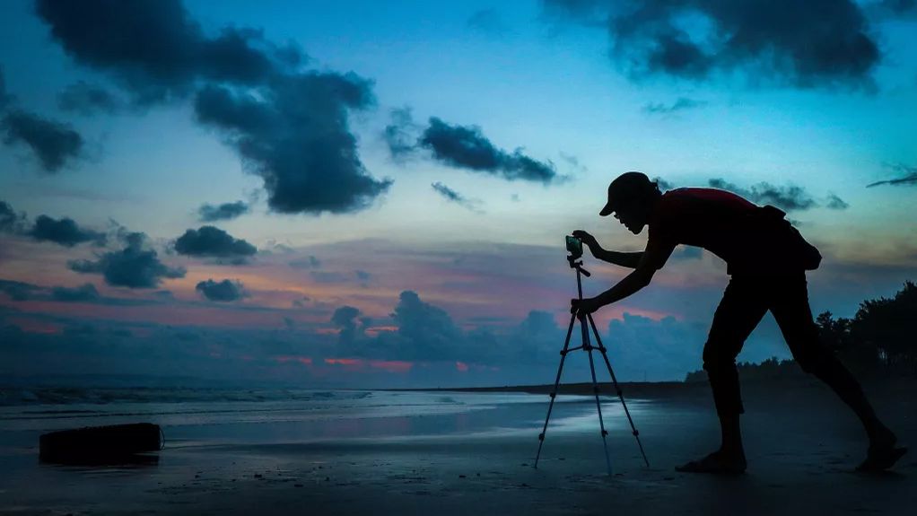 Smartphone astrophotography: Image shows man adjusting phone on tripod, which is pointing at night sky