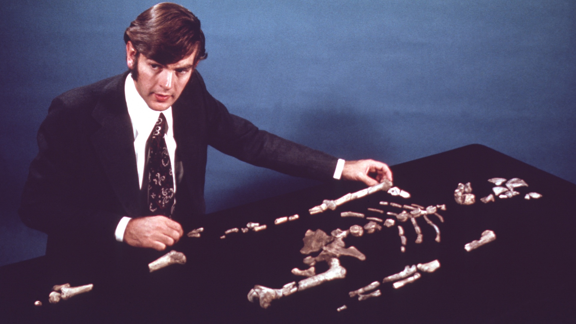 An old photo of Donald Johanson standing over Lucy's bones laid out on a table