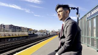 a man in a suit waits for the subway in a still from the documentary heightened scrutiny