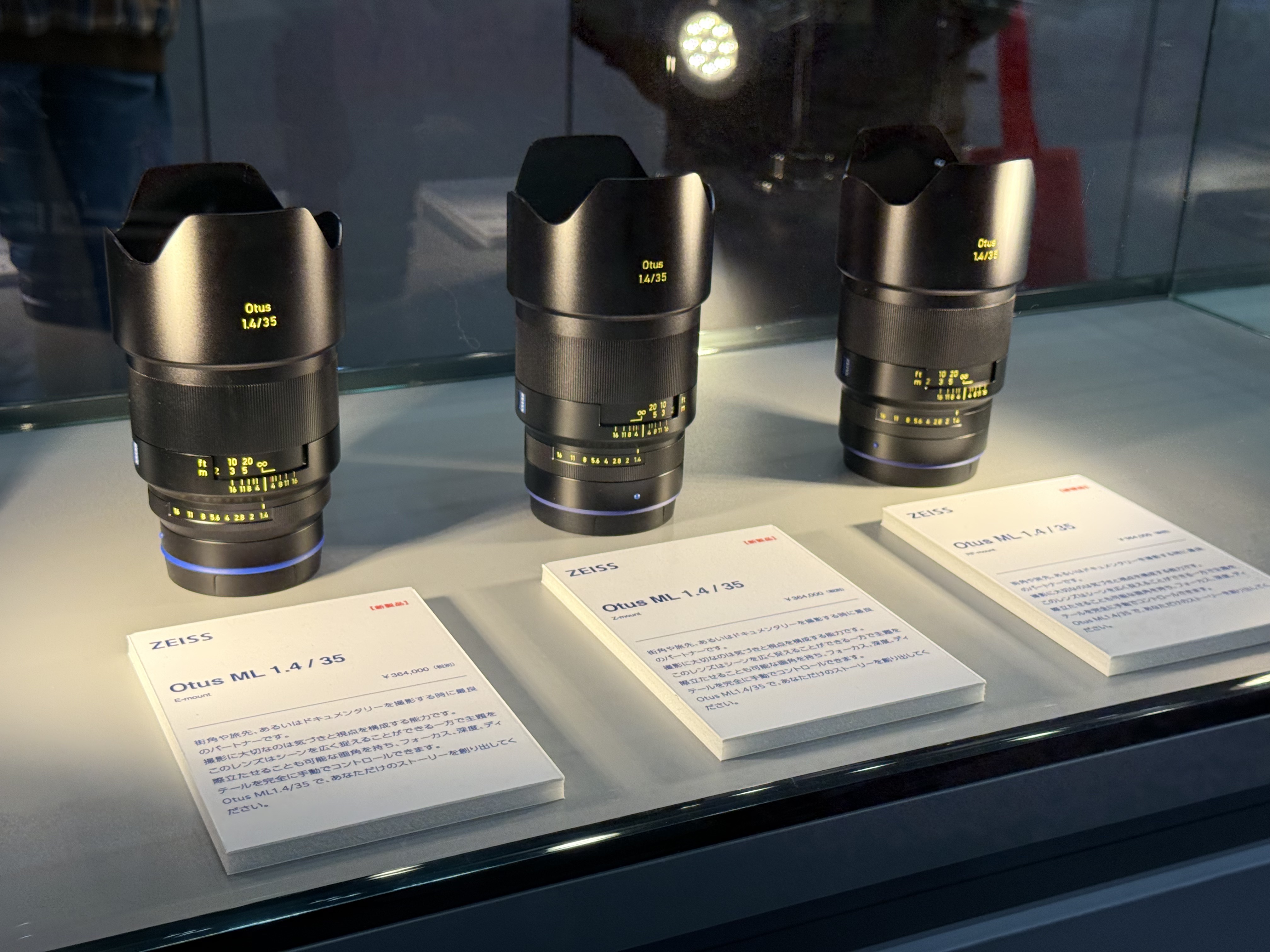 Three Zeiss Otus f/1.4 lenses for mirrorless cameras, inside a glass cabinet at the CP+ 2026 show