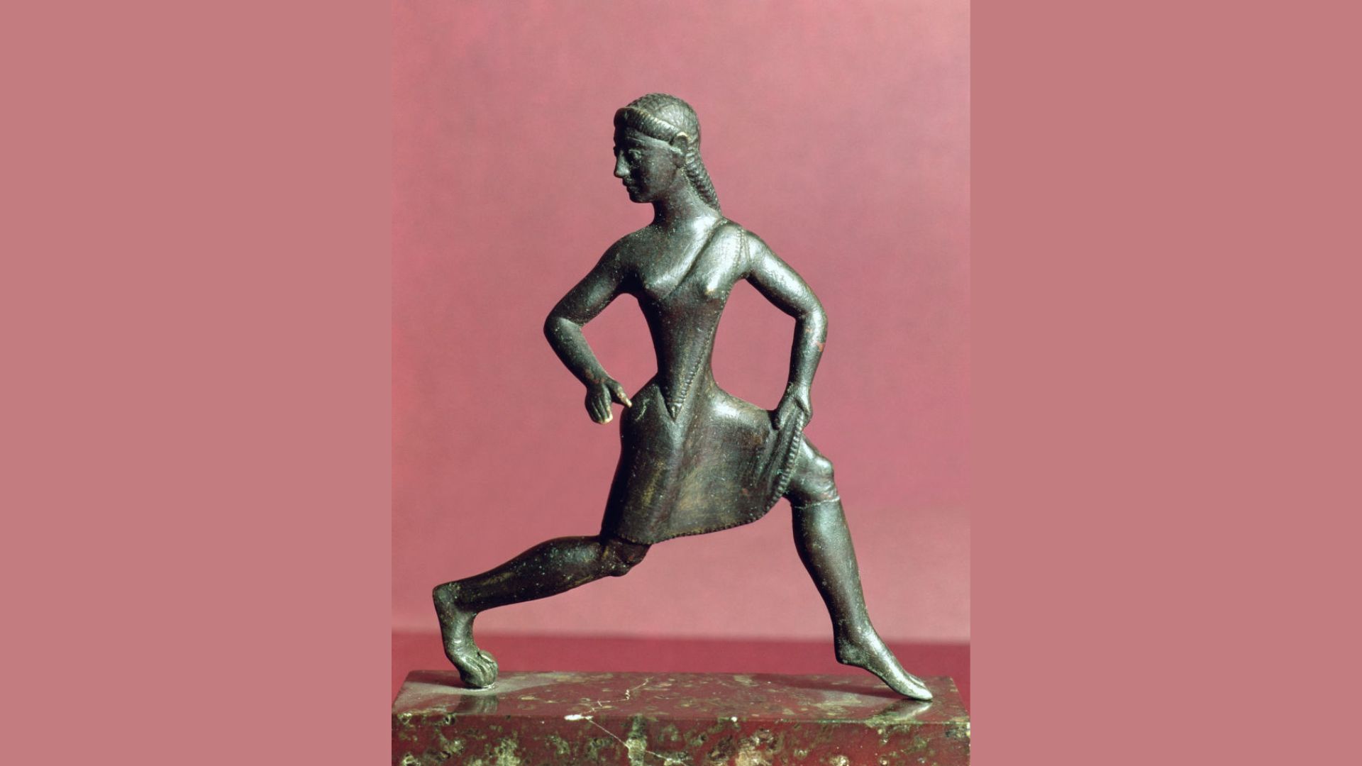 Photo of an ancient statuette of a woman mounted on a slab of red marble.