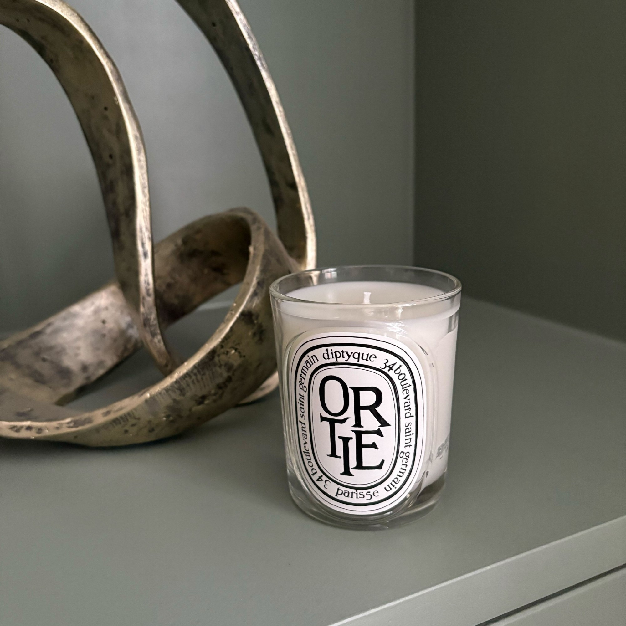 Diptyque's Ortie candle on Sophie King's green living room alcove shelving with a decorative sculpture next to it