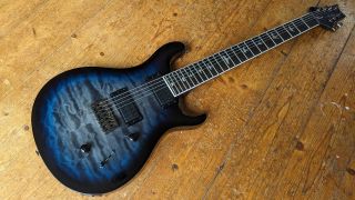 A PRS SE Mark Holcomb SVN 7-string electric guitar on a wooden floor