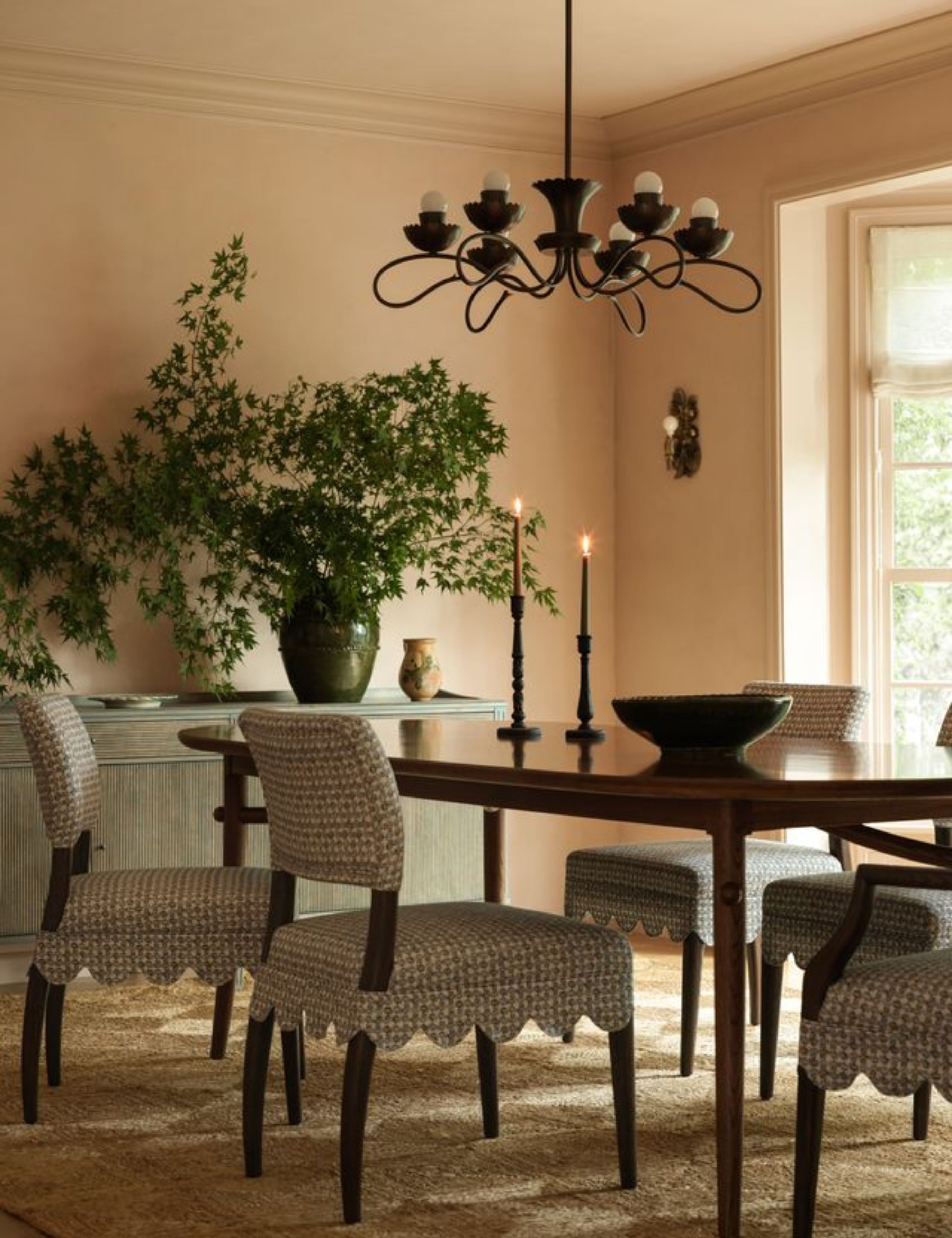 Playful dining room featuring scallop-bordered dining chairs, a wooden table, and sculptural burnished brass chandelier.