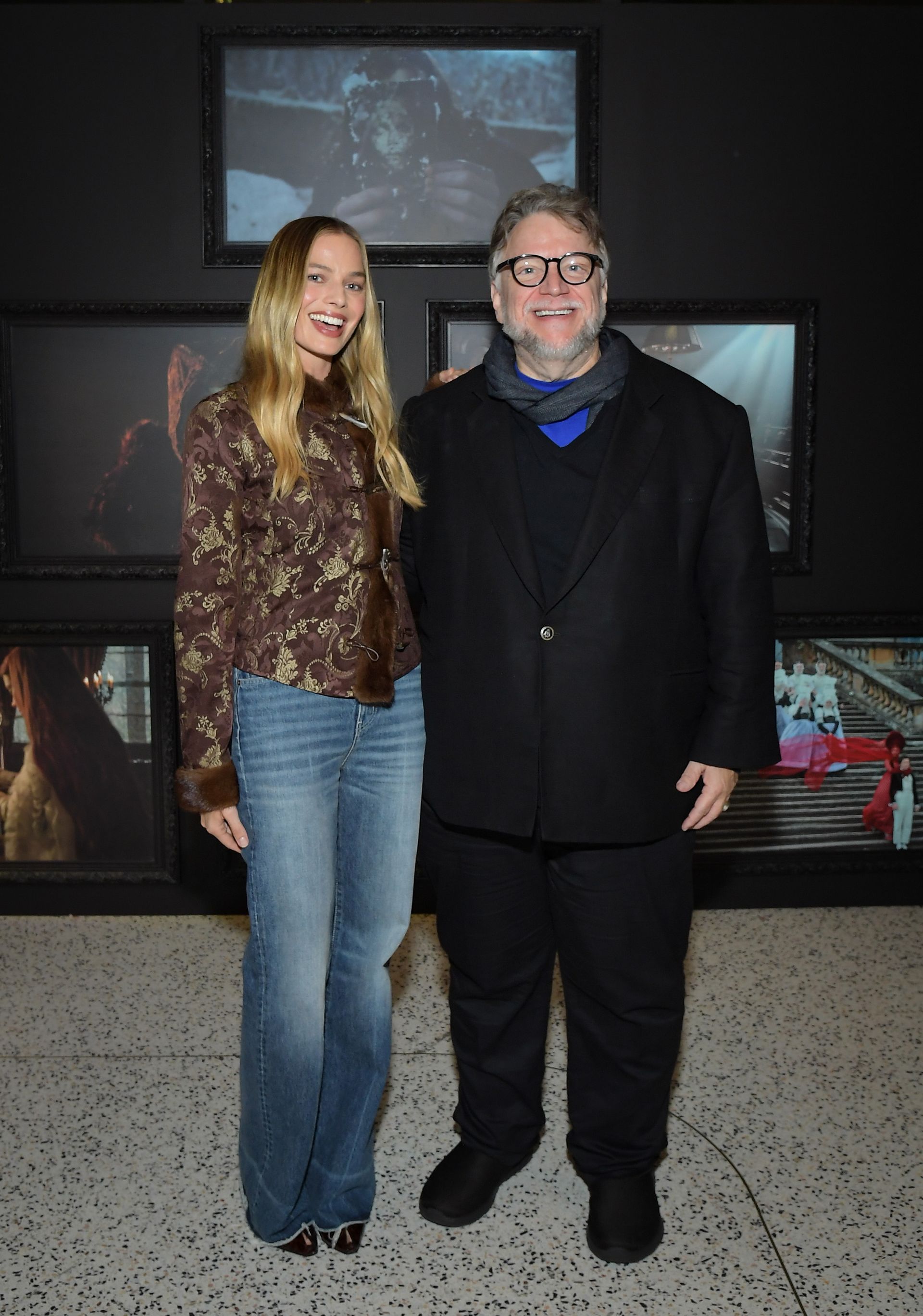 Margot Robbie wear mid-wash blue jeans with brown pointed-toe heels and a brown printed jacket.
