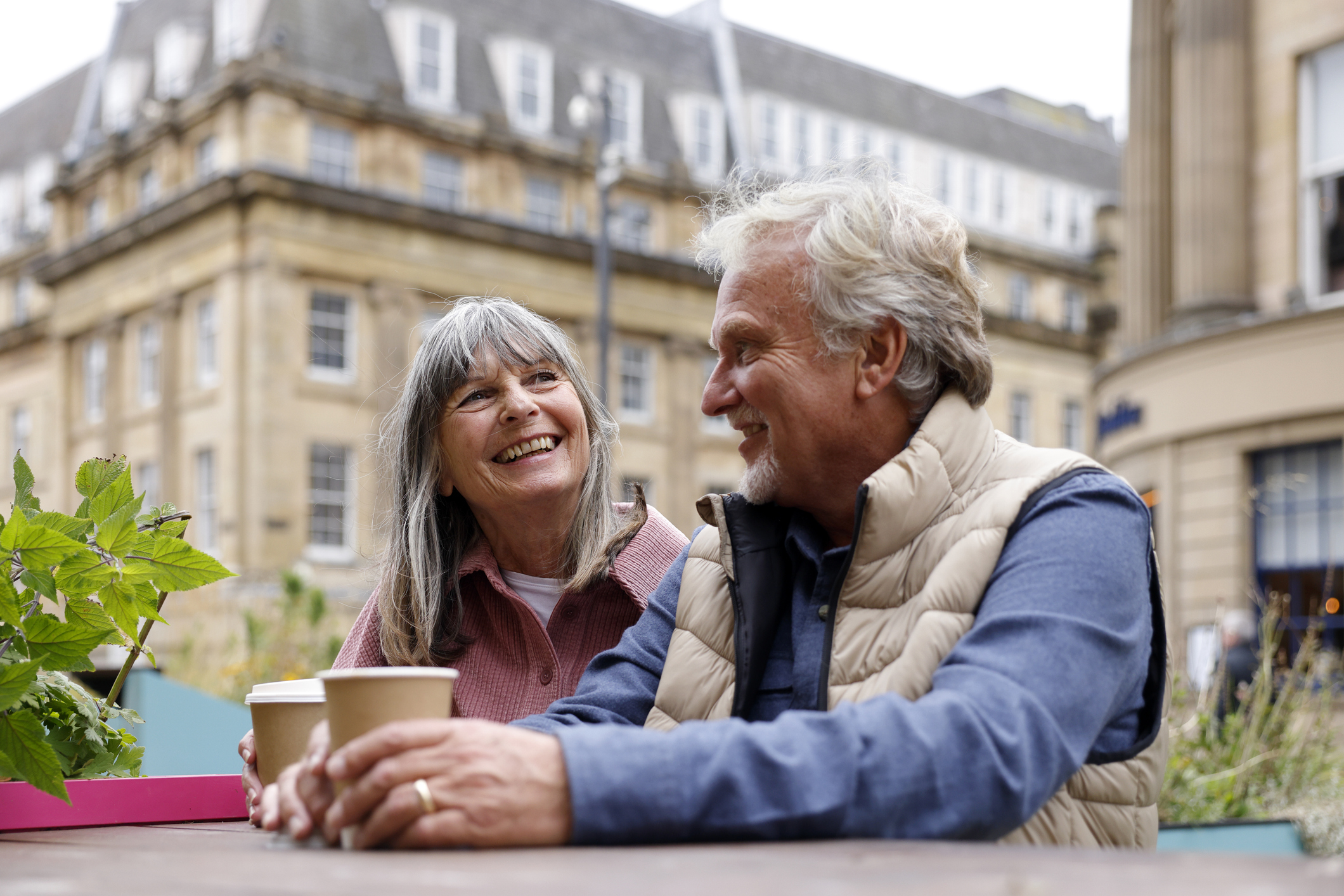 A happy senior couple enjoy a moment together while seated at an outdoor city caf&eacute; during a city break. 