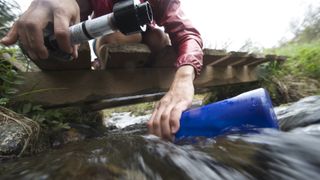 A hiker filters water from a stream