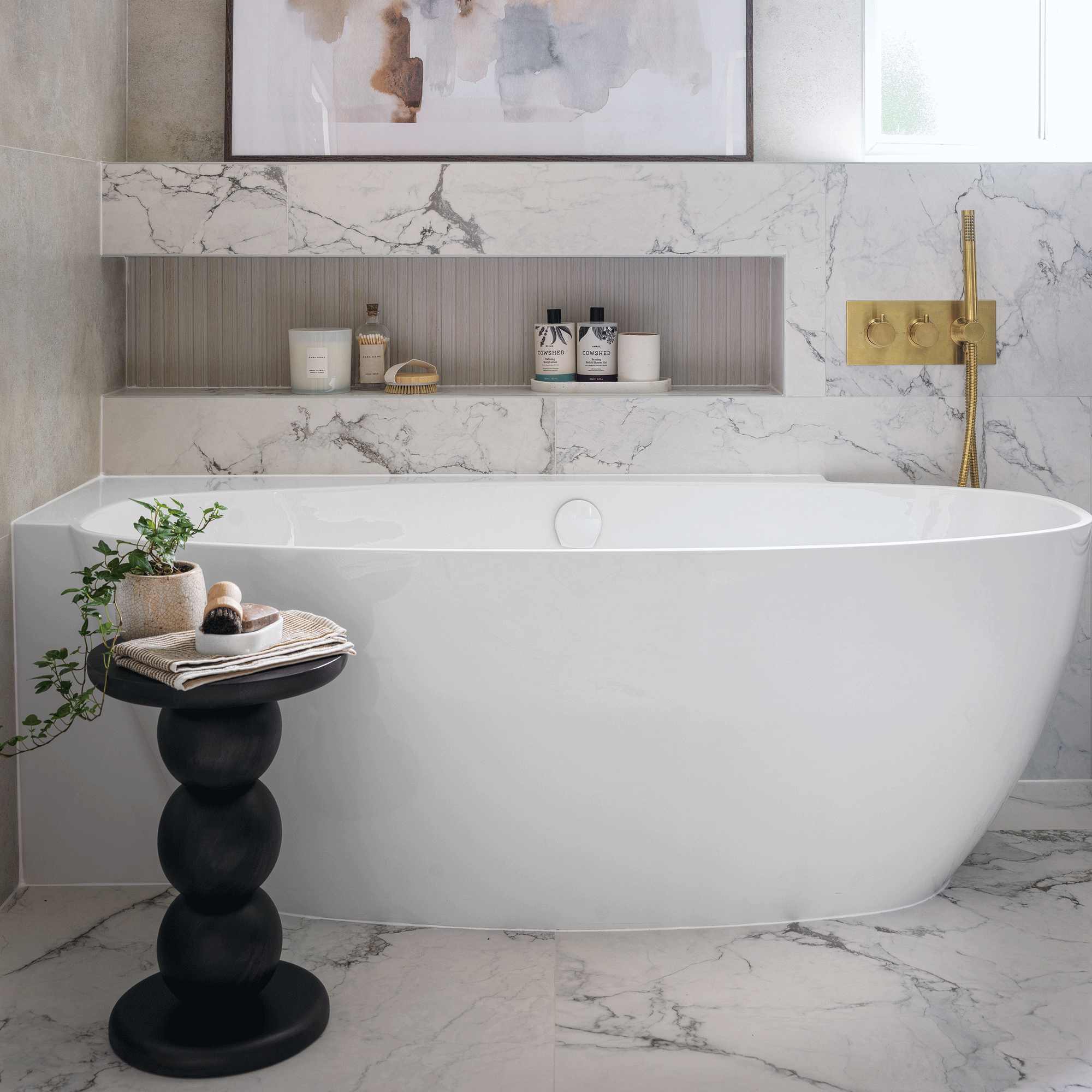 a marble-covered monochrome bathroom with a large bath tub and a black statement side table