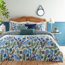 A blue and white bedroom with a bed with a blue and green patterned duvet cover