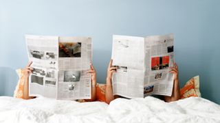 oung couple reading newspaper on bed