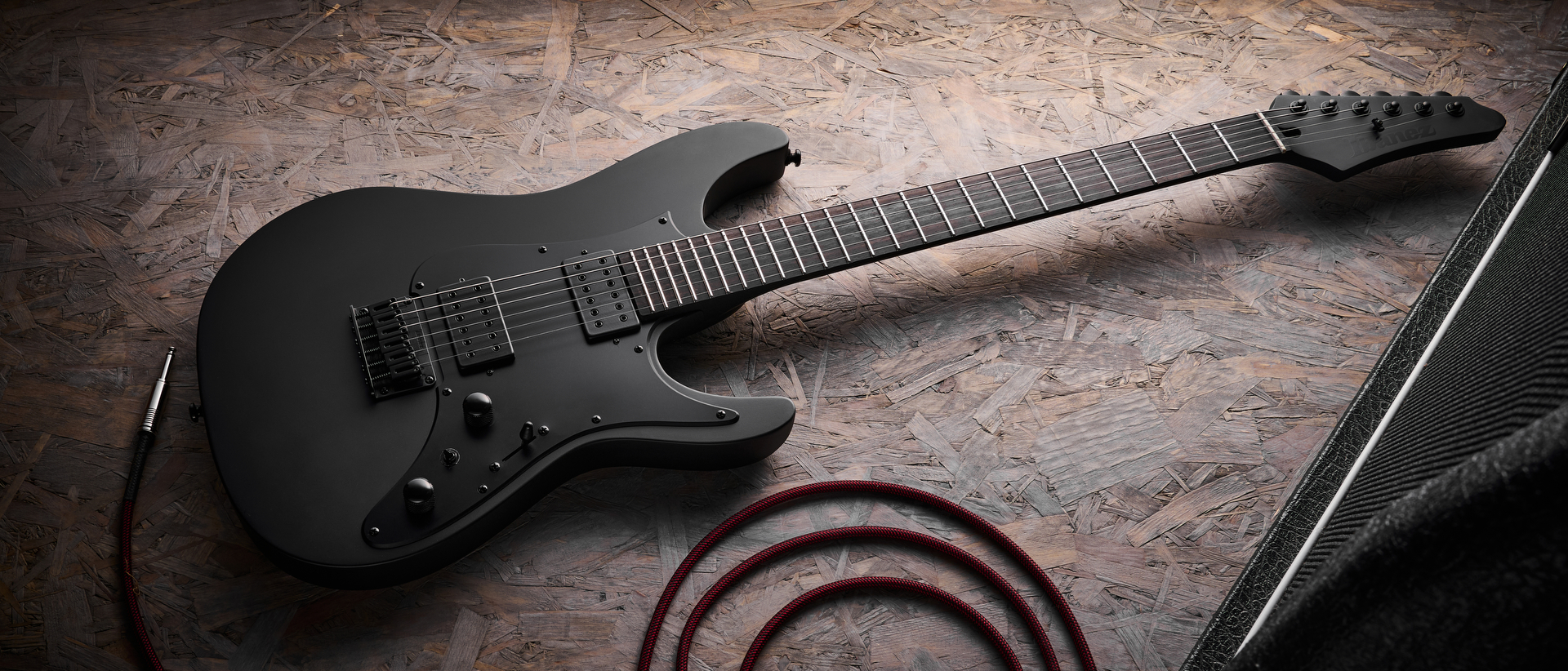 An Ibanez Iron Label AZ41B1 electric guitar on a sheet of wood with a guitar cable