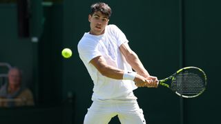 Carlos Alcaraz plays a backhand all in white on court at Wimbledon 2024.