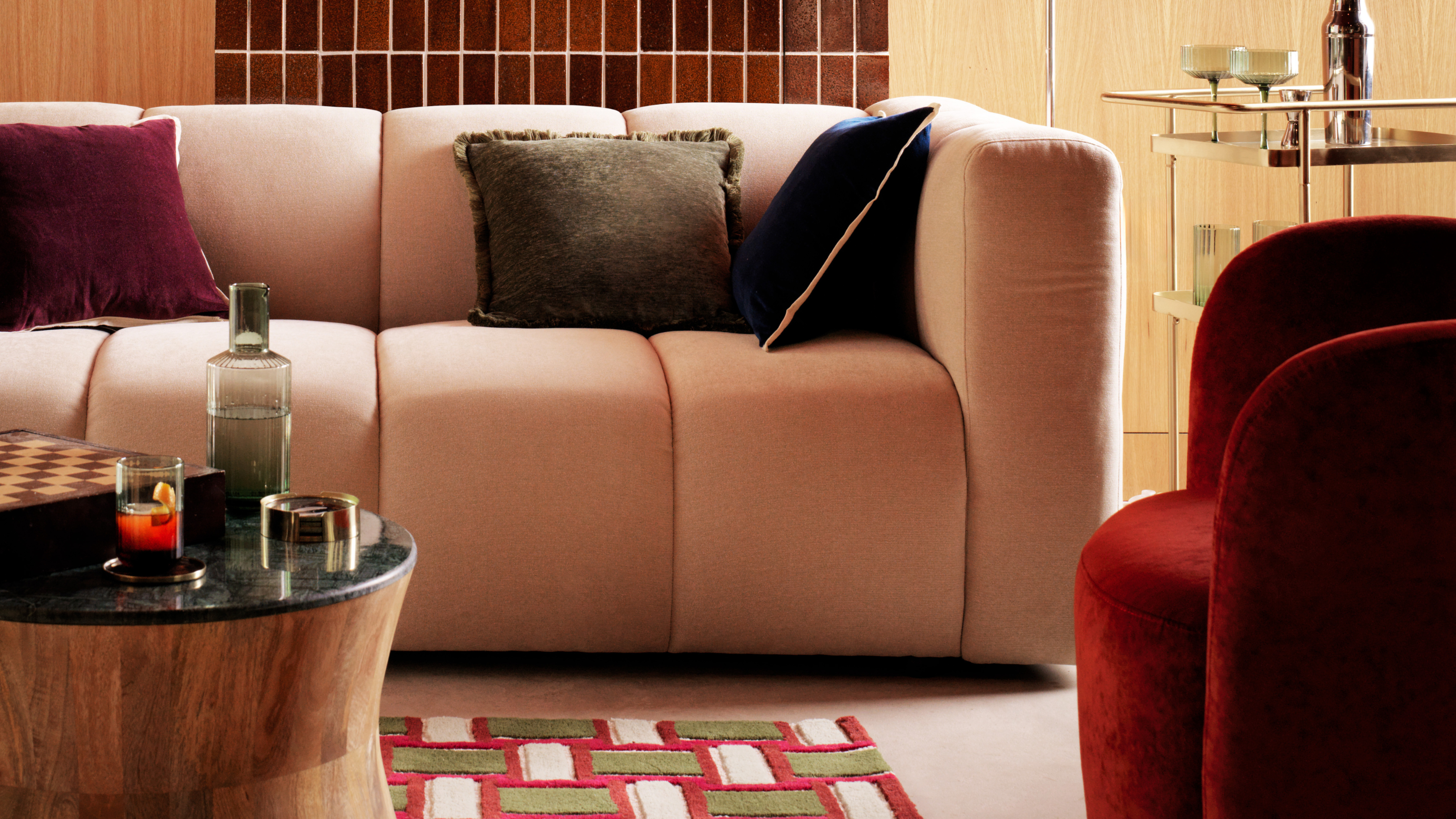 Habitat cream modular sofa in a 70's inspired space. There is a red and green geometric rug, red swivel chair and curved, wooden coffee table.