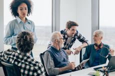 Diverse office employees chat around a meeting table.