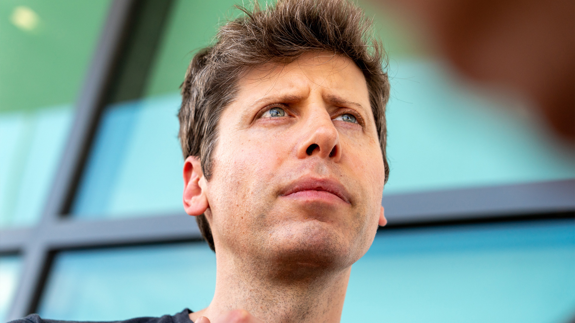 Sam Altman&#039;s face with glass windows behind him.