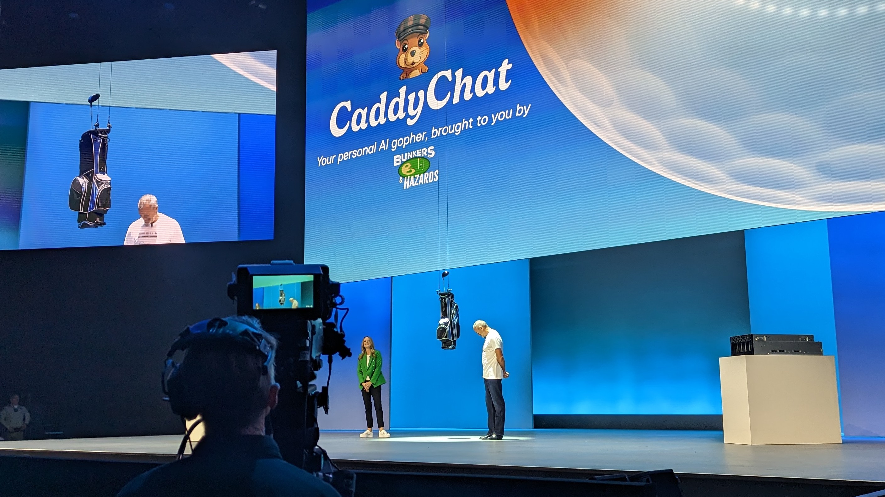 Co-COO Jeff Clarke and chief digital officer and CIO Jen Felch on stage, with a golf bag containing clubs being lowered onto stage via wires and a stylized logo on a large screen behind them showing a chipmunk the word 'CaddyChat'.